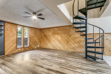  living room with stairs, a textured ceiling, wooden walls, wood finished floors, and a ceiling fan