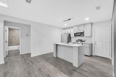 Kitchen featuring appliances with stainless steel finishes, an island with sink, light wood finished floors, recessed lighting, and gray cabinets