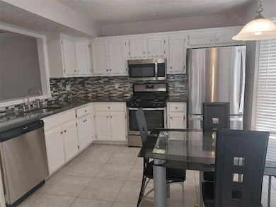 Kitchen with stainless steel appliances, dark countertops, backsplash, white cabinets, and a textured ceiling