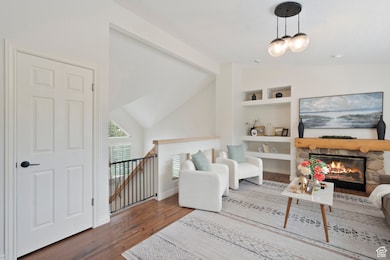 Living area featuring an upstairs landing, lofted ceiling, a stone fireplace, and dark wood finished floors