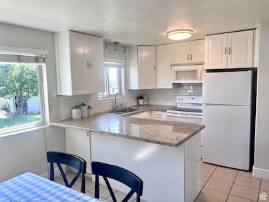 Kitchen featuring white appliances, white cabinets, light stone countertops, decorative backsplash, and a textured ceiling