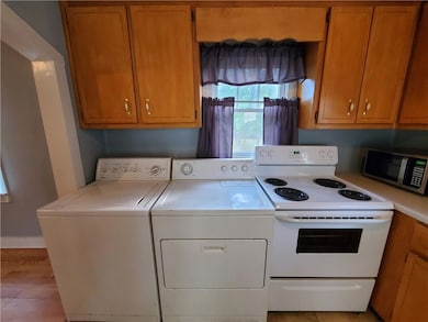 Kitchen with white electric stove, independent washer and dryer, stainless steel microwave, light countertops, and brown cabinetry