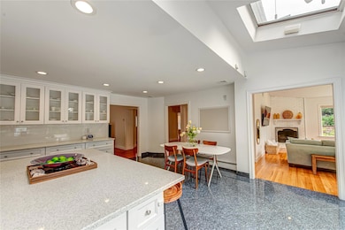 Kitchen featuring white cabinetry, glass insert cabinets, light quartz stone countertops, granite tiled floors, and a skylight