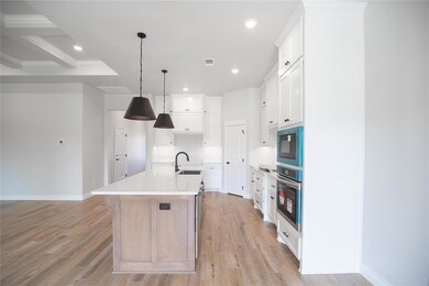 Kitchen with stainless steel oven, black microwave, a center island with sink, recessed lighting, and light wood finished floors