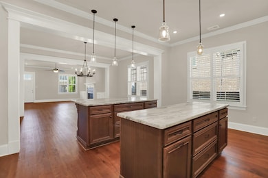 Kitchen featuring a kitchen island, baseboards, dark wood-style flooring, crown molding, and decorative light fixtures