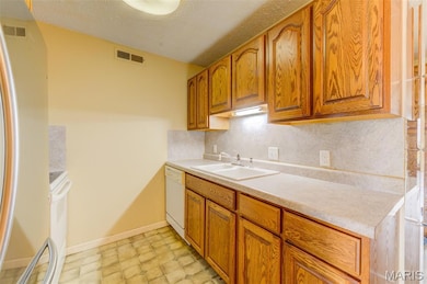 Kitchen with backsplash, white appliances, light countertops, a textured ceiling, and brown cabinets