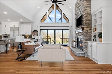 Living room with a ceiling fan, a stone fireplace, high vaulted ceiling, and light wood-type flooring