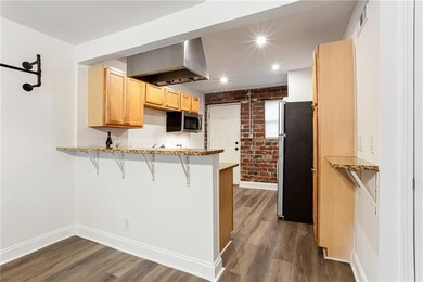 Kitchen featuring stainless steel appliances, wall chimney exhaust hood, a peninsula, light brown cabinets, and baseboards