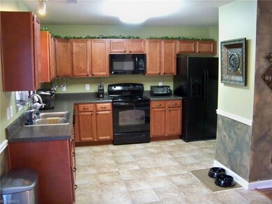 Large kitchen features cherry colored cabinets and black appliances - they contrast nicely to the light flooring...