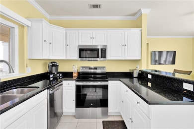 Kitchen with stainless steel appliances, ornamental molding, dark stone countertops, and white cabinets
