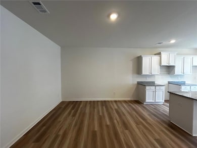 Kitchen featuring dark wood-style flooring, white cabinetry, and light stone countertops