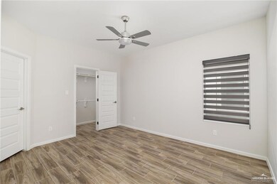 Unfurnished bedroom featuring a spacious closet, wood finished floors, a ceiling fan, and baseboards
