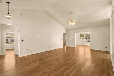Unfurnished living room featuring ceiling fan, high vaulted ceiling, wood finished floors, and baseboards