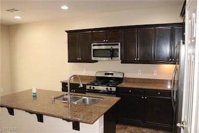 Kitchen with stainless steel appliances, a breakfast bar area, recessed lighting, dark stone countertops, and an island with sink