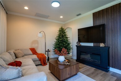 Living room with crown molding, wood finished floors, a glass covered fireplace, and recessed lighting