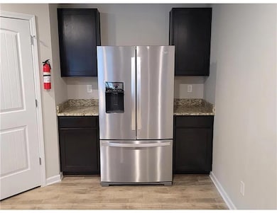Kitchen featuring stainless steel refrigerator with ice dispenser, light wood-style flooring, and light stone countertops
