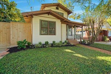 Charming single-story craftsman home with a welcoming front porch, surrounded by lush greenery and a well-maintained lawn. The house features a wooden fence for privacy and a brick pathway leading to the entrance. Ideal for cozy living in a serene neighborhood.