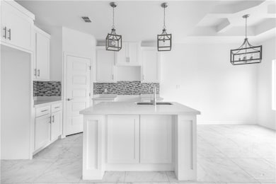 Kitchen featuring white cabinets, sink, backsplash, and hanging light fixtures
