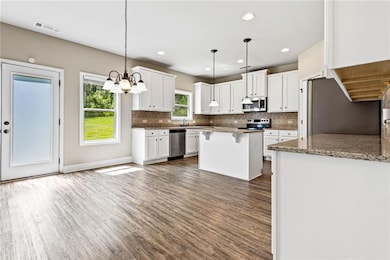 Kitchen with stainless steel appliances, dark wood finished floors, white cabinets, tasteful backsplash, and recessed lighting