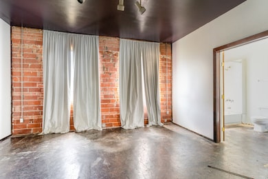Unfurnished room featuring brick wall, concrete flooring, and rail lighting