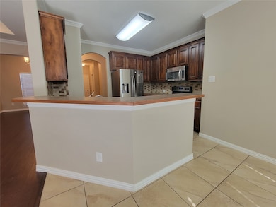 Kitchen featuring decorative backsplash, arched walkways, stainless steel appliances, a peninsula, and dark brown cabinets