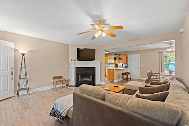 Living area featuring a ceiling fan, light wood finished floors, a fireplace with flush hearth, and a textured ceiling