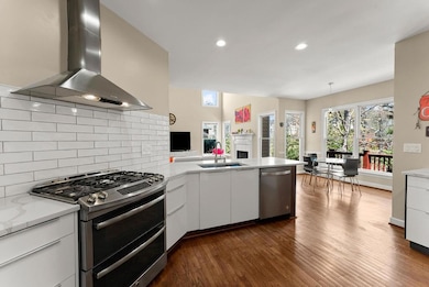 Kitchen with stainless steel appliances, a sink, a peninsula, a fireplace, and ventilation hood