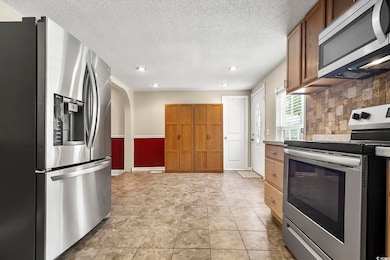 Kitchen with stainless steel appliances, recessed lighting, a textured ceiling, brown cabinetry, and decorative backsplash