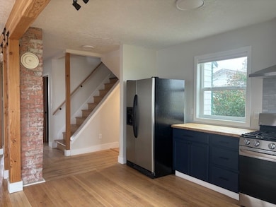 Kitchen with appliances with stainless steel finishes, blue cabinets, light wood-type flooring, a textured ceiling, and wall chimney range hood