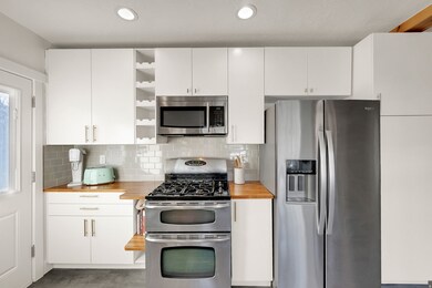 Kitchen featuring appliances with stainless steel finishes, open shelves, white cabinetry, butcher block countertops, and recessed lighting