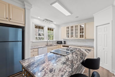 Kitchen with freestanding refrigerator, a kitchen bar, dark stone counters, crown molding, and a center island