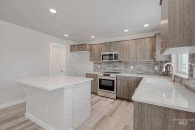 Kitchen with tasteful backsplash, appliances with stainless steel finishes, modern cabinets, light stone countertops, and recessed lighting