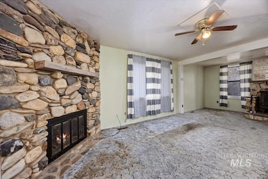 Unfurnished living room featuring a stone fireplace, carpet floors, a textured ceiling, and a ceiling fan
