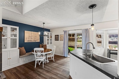 Kitchen with a textured ceiling, dark countertops, dark wood-style floors, a chandelier, and pendant lighting