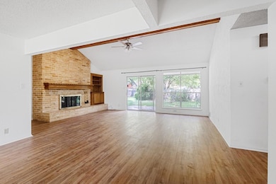 Unfurnished living room featuring light wood finished floors, a brick fireplace, a ceiling fan, and a textured ceiling