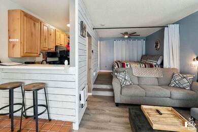 Living room with light wood-style floors, ceiling fan, wooden walls, and a textured ceiling