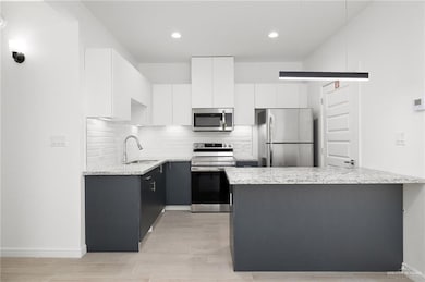 Kitchen with white cabinetry, stainless steel appliances, backsplash, modern cabinets, and light stone countertops
