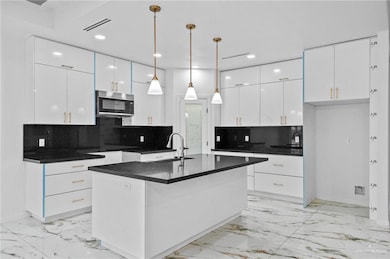Kitchen with a sink, dark countertops, visible vents, stainless steel microwave, and marble finish floor