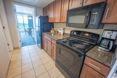 Kitchen featuring black appliances, a sink, dark stone counters, brown cabinetry, and light tile patterned floors