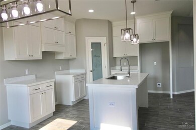 Kitchen with a sink, wood finish floors, a kitchen island with sink, baseboards, and recessed lighting