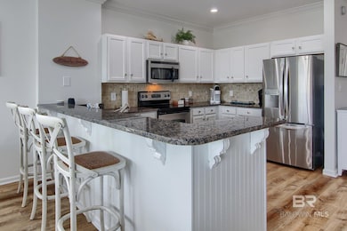 Kitchen featuring appliances with stainless steel finishes, light wood-type flooring, tasteful backsplash, a peninsula, and crown molding