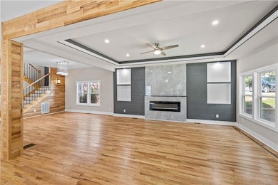 Unfurnished living room with a tray ceiling, light wood-style flooring, stairway, ceiling fan, and recessed lighting