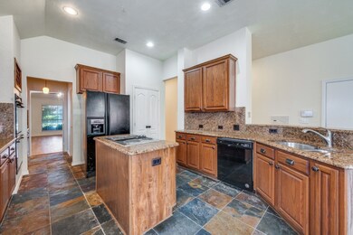 Kitchen featuring brown cabinetry, light stone counters, tasteful backsplash, black appliances, and a kitchen island