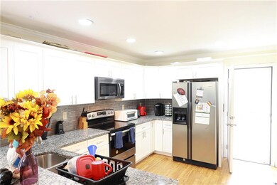 Kitchen with stainless steel appliances, ornamental molding, decorative backsplash, white cabinets, and light wood finished floors