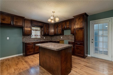Kitchen featuring a chandelier, light wood finished floors, dark brown cabinets, and backsplash