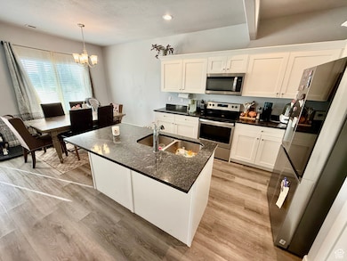 Kitchen with appliances with stainless steel finishes, white cabinets, light wood-style flooring, hanging light fixtures, and recessed lighting