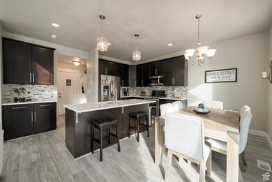 Kitchen with stainless steel appliances, tasteful backsplash, a breakfast bar area, hanging light fixtures, and a kitchen island with sink