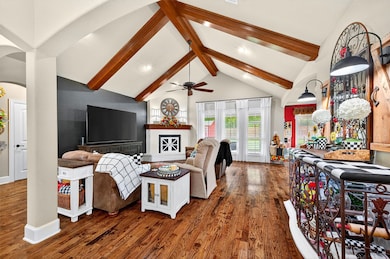Living room with wood finished floors, beam ceiling, high vaulted ceiling, arched walkways, and a fireplace with raised hearth