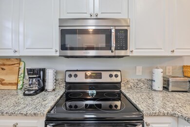 Kitchen with stainless steel appliances, light stone countertops, and white cabinetry