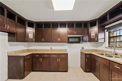 Kitchen featuring open shelves, stainless steel microwave, a sink, light stone countertops, and dark brown cabinetry